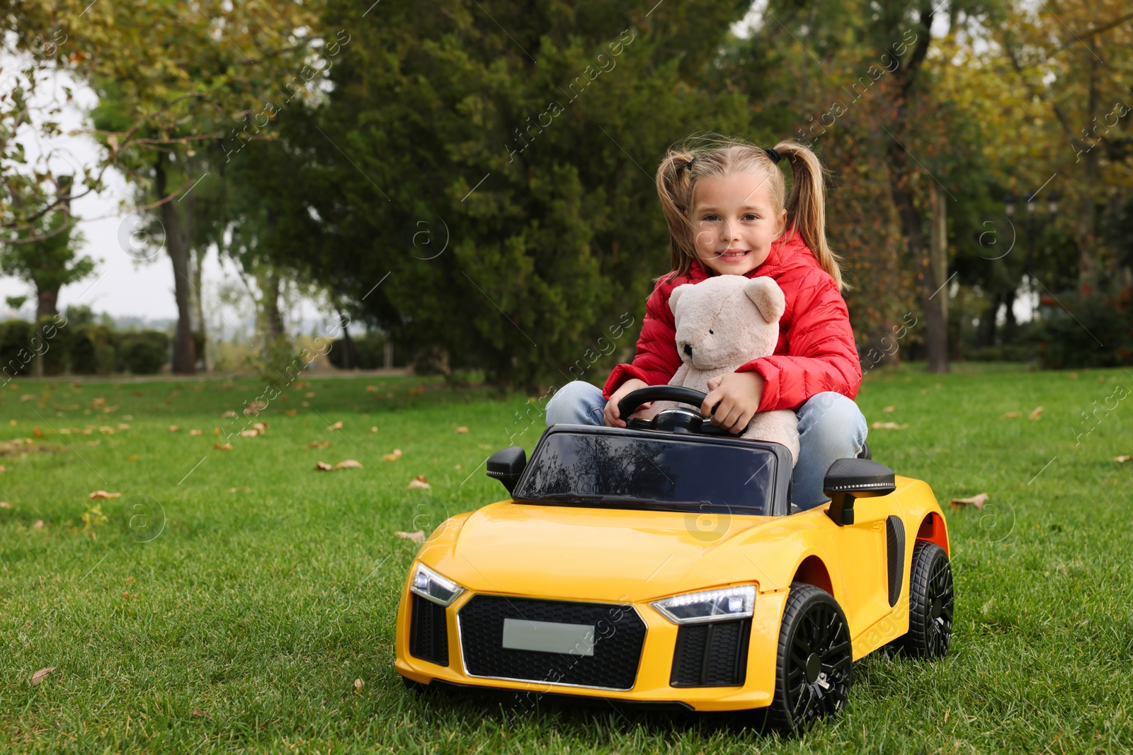 Photo of Cute little girl playing with toy bear and children's car in park. Space for text