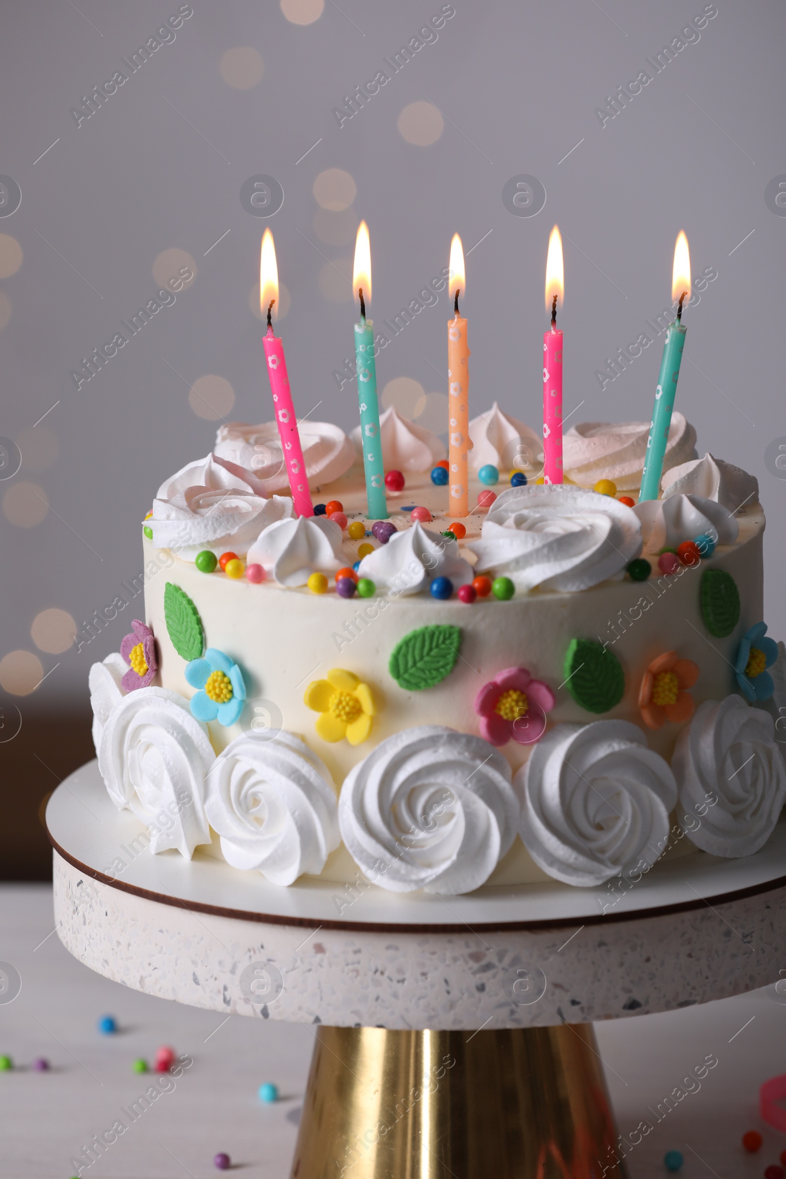 Photo of Delicious birthday cake with party decor on stand against blurred festive lights, closeup