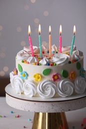 Photo of Delicious birthday cake with party decor on stand against blurred festive lights, closeup