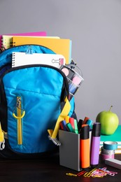 Photo of Children's backpack and different school stationery on wooden table against grey background