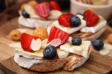 Photo of Tasty sandwiches with brie cheese, fresh berries and almond flakes on wooden board, closeup