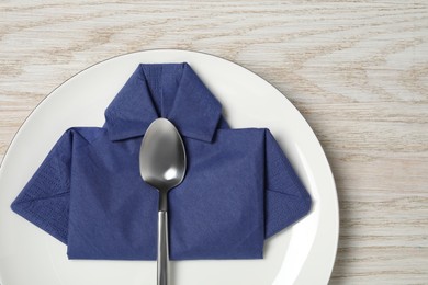 Photo of Plate with shirt made of paper napkin and spoon on wooden table, top view. Business lunch concept