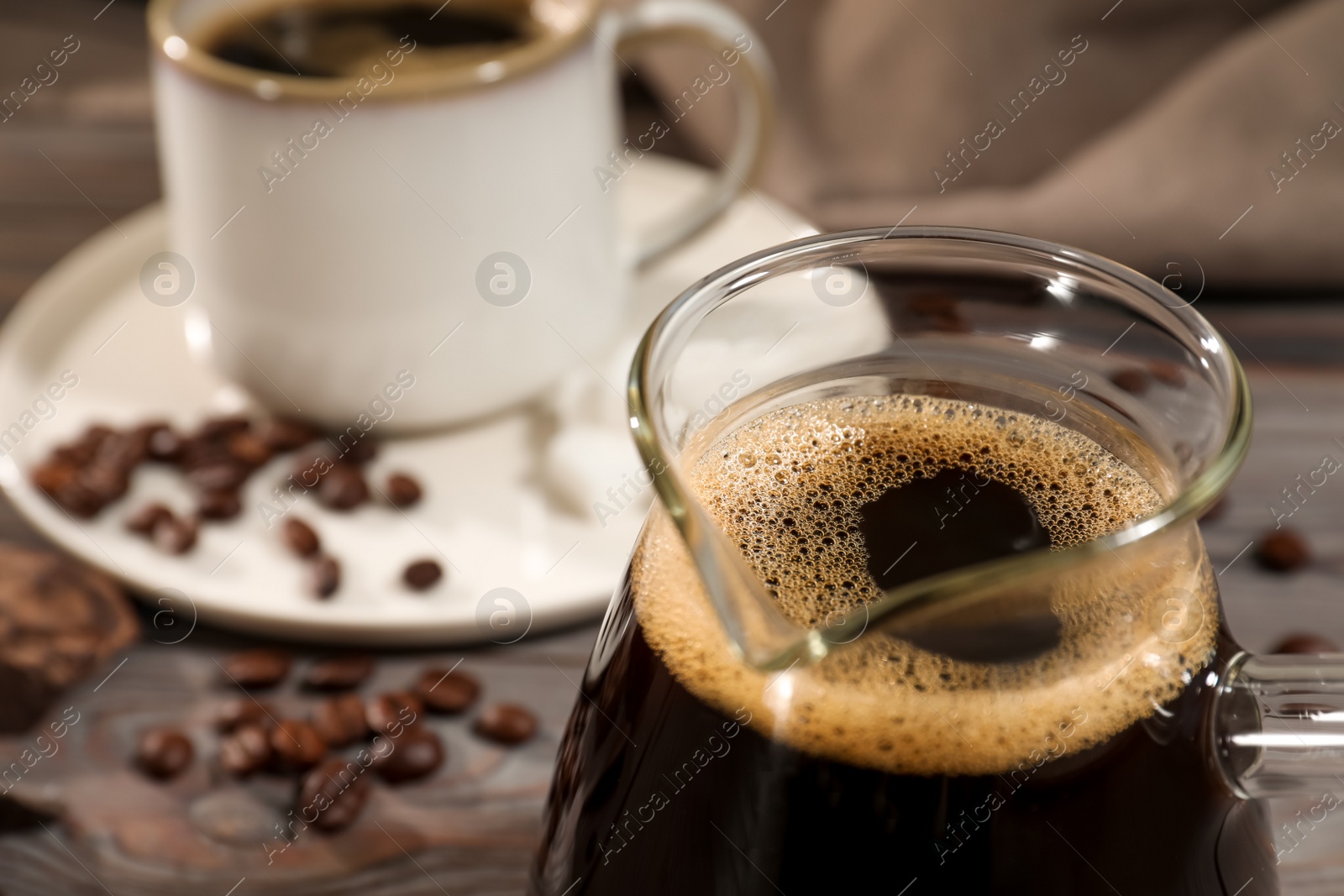 Photo of Glass turkish coffee pot with hot drink on wooden table, closeup. Space for text