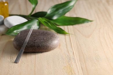 Photo of Acupuncture needles, spa stones and green leaves on wooden table, space for text