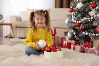 Cute little girl with box of Christmas balls at home