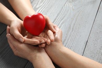 Photo of Young and elderly women holding red heart at grey wooden table, closeup