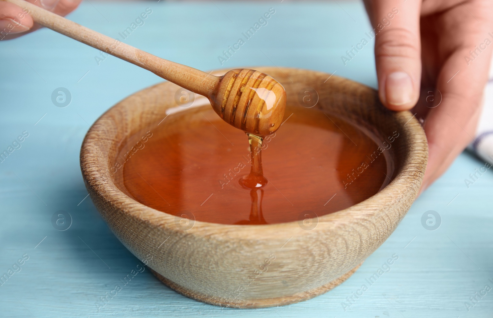 Photo of Woman with honey and dipper at blue wooden table, closeup