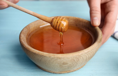 Photo of Woman with honey and dipper at blue wooden table, closeup