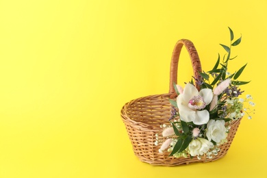 Photo of Wicker basket decorated with beautiful flowers on yellow background, space for text. Easter item