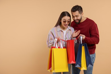 Photo of Man showing shopping bag with purchase to his girlfriend on beige background. Space for text