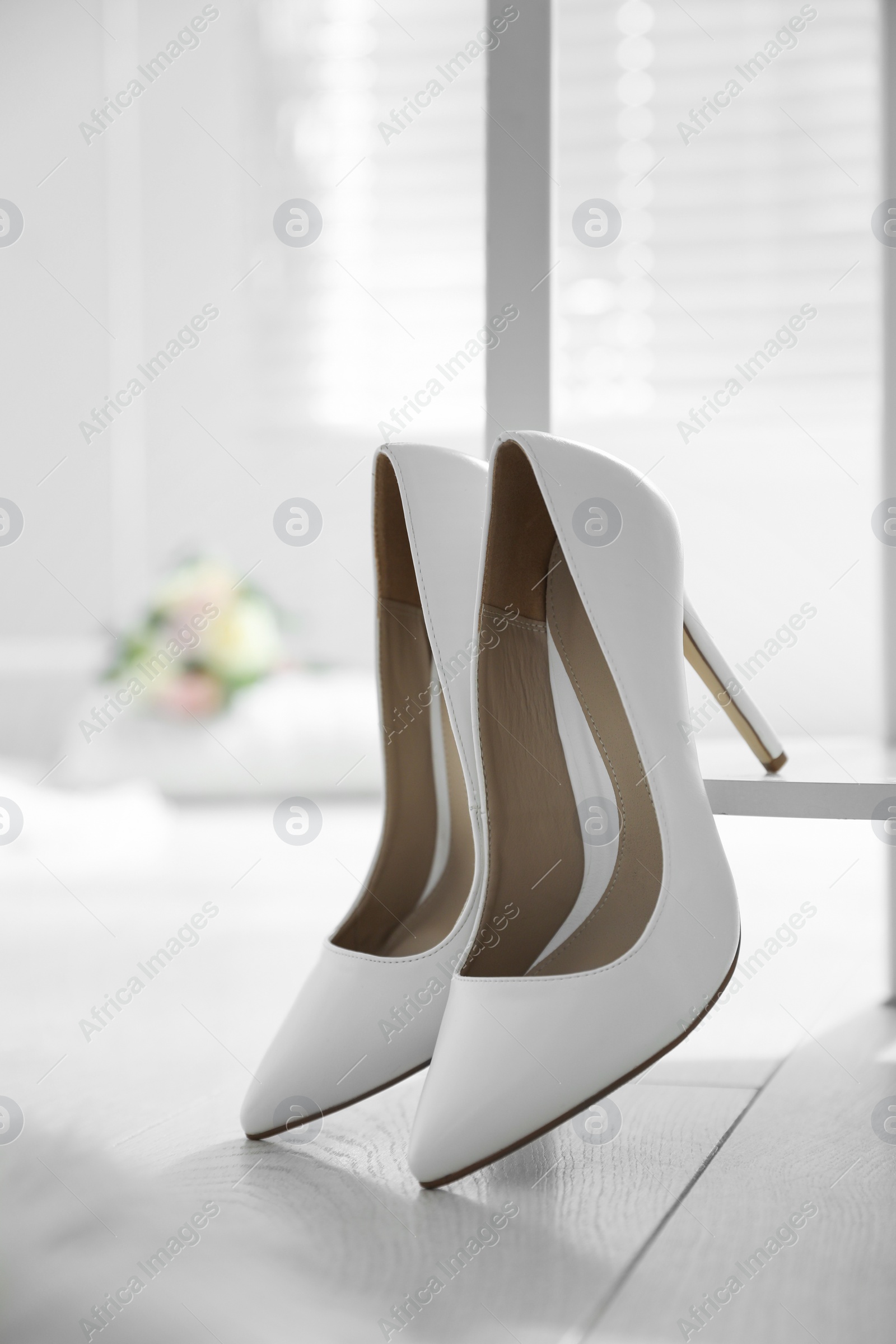 Photo of Pair of white wedding high heel shoes indoors, closeup