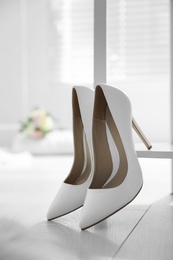 Pair of white wedding high heel shoes indoors, closeup