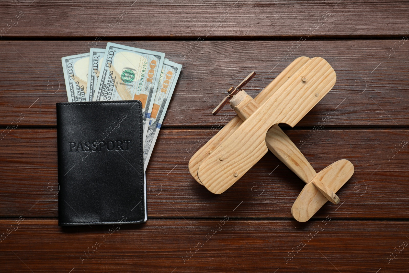 Photo of Dollars, passport and model of plane on wooden table, flat lay. Business trip