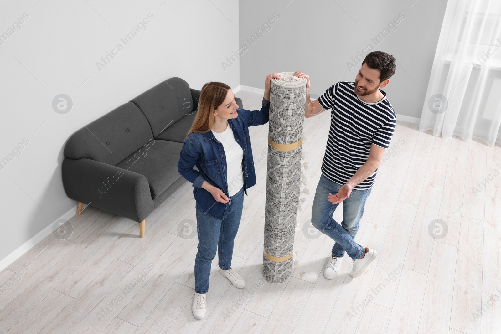 Photo of Smiling couple holding rolled carpet in room