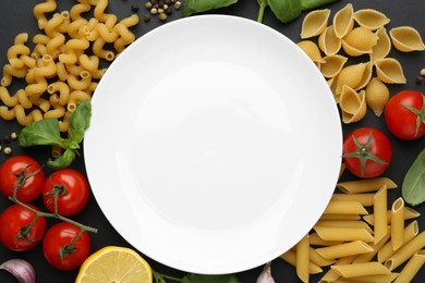 Plate surrounded by different types of pasta and products on black background, flat lay. Space for text