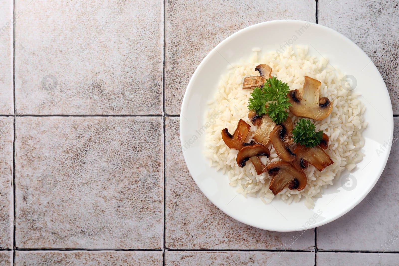 Photo of Delicious rice with parsley and mushrooms on tiled table, top view. Space for text
