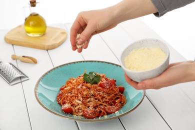 Food stylist adding grated cheese to spaghetti at white wooden table in photo studio, closeup