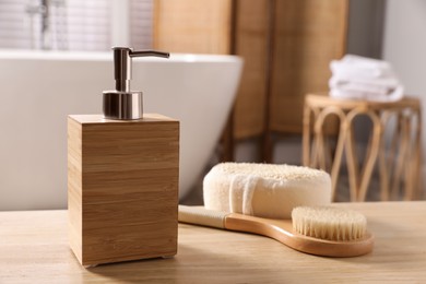 Dispenser of liquid soap, brush and loofah on wooden table in bathroom, space for text