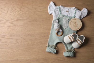 Photo of Baby clothes, shoes and toy on wooden background, flat lay. Space for text