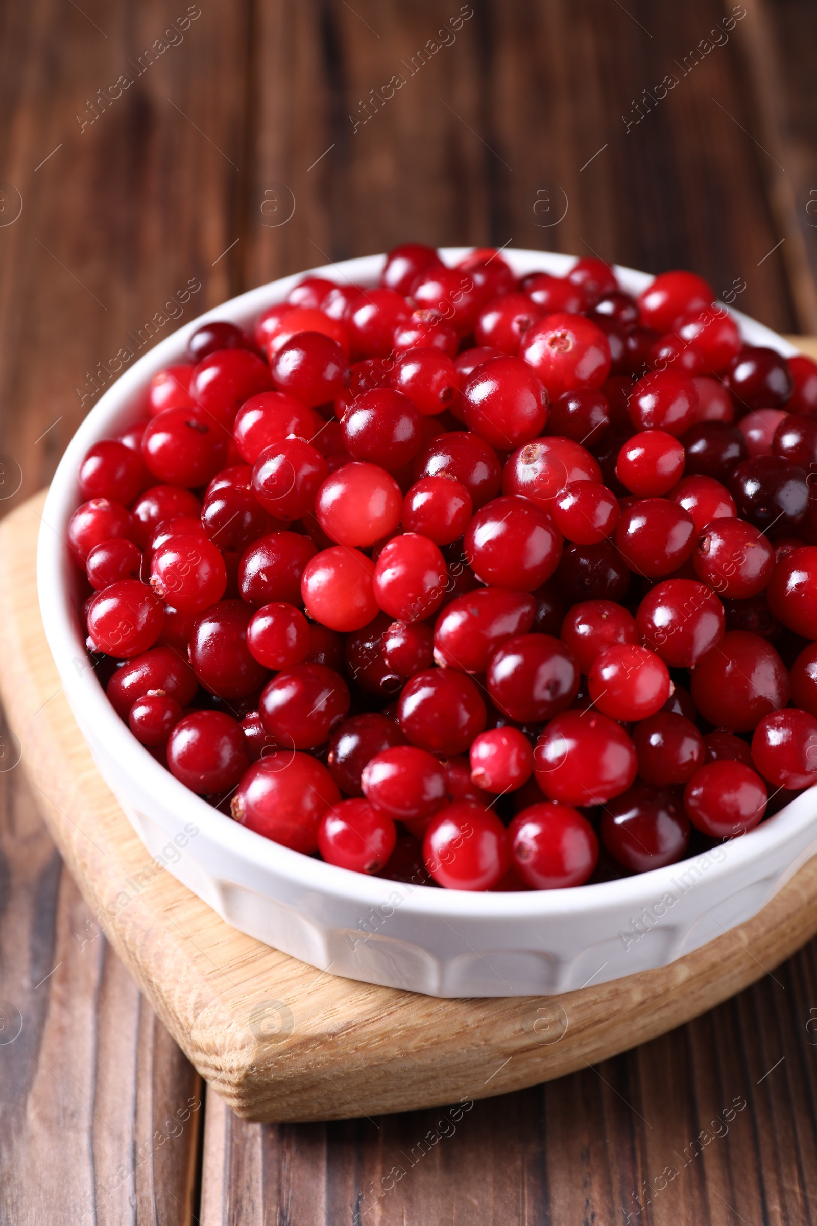 Photo of Fresh ripe cranberries in bowl on wooden table, closeup