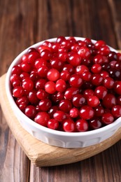 Photo of Fresh ripe cranberries in bowl on wooden table, closeup