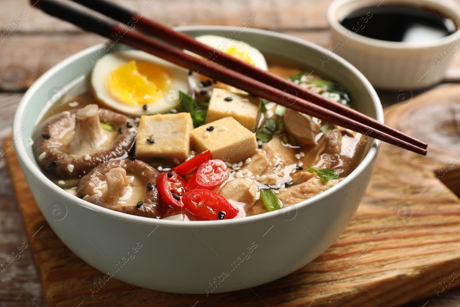 Photo of Noodle soup. Bowl of delicious ramen and chopsticks on wooden table, closeup