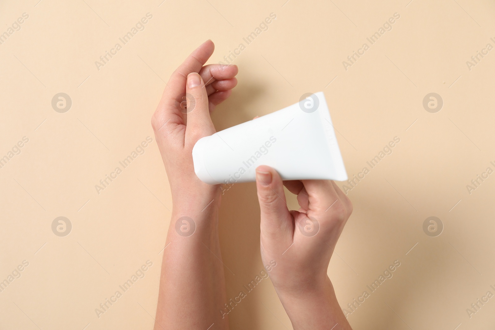 Photo of Woman with tube of hand cream on beige background, top view