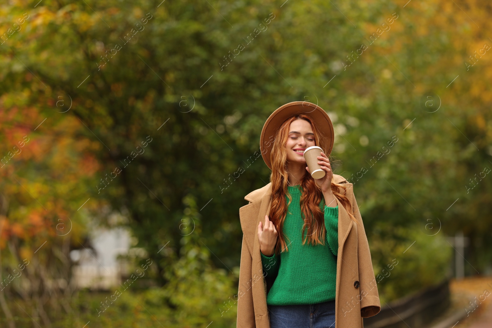 Photo of Beautiful woman drinking coffee from paper cup in autumn park. Space for text