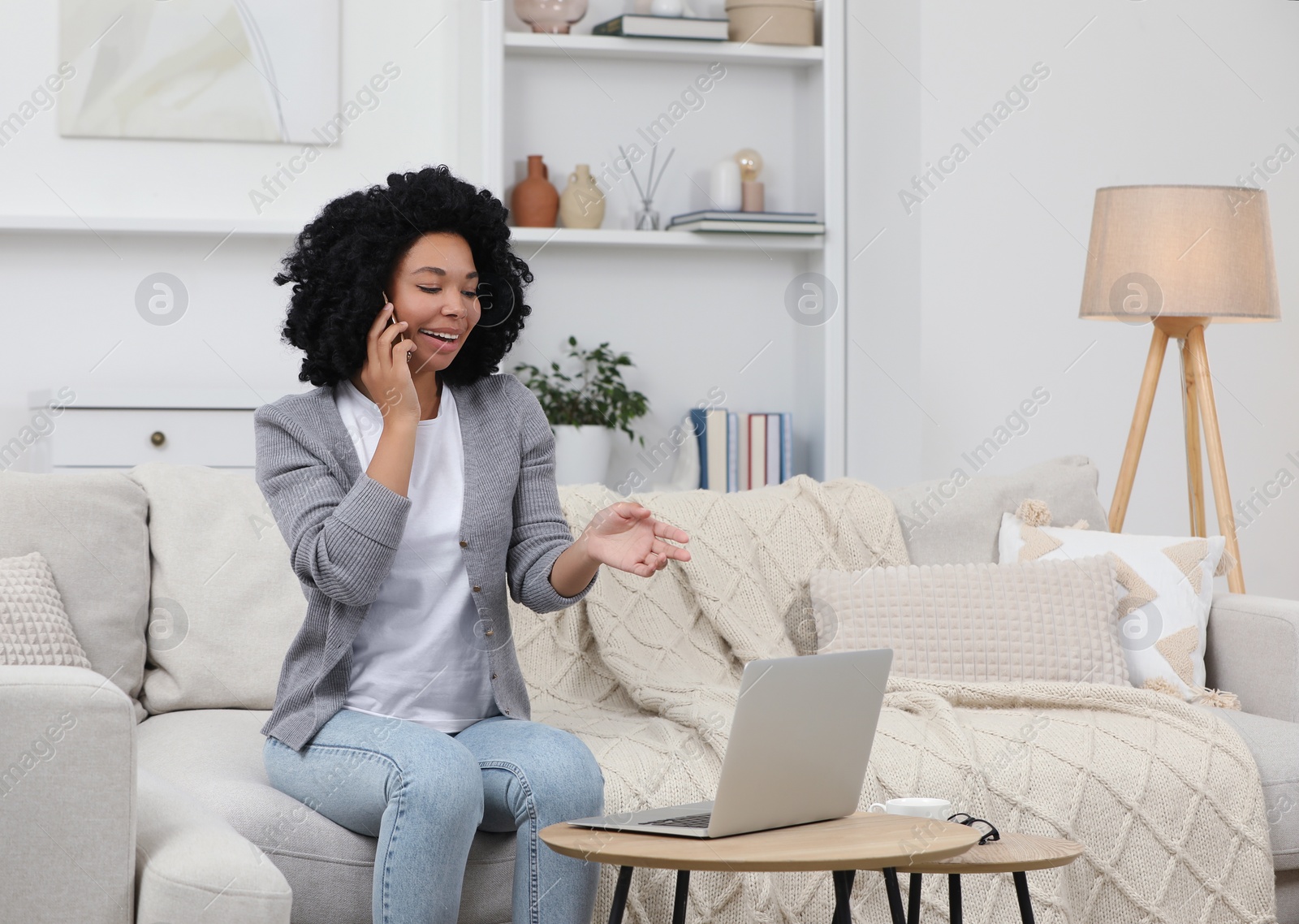 Photo of Happy young woman talking on phone while using laptop at coffee table indoors. Space for text