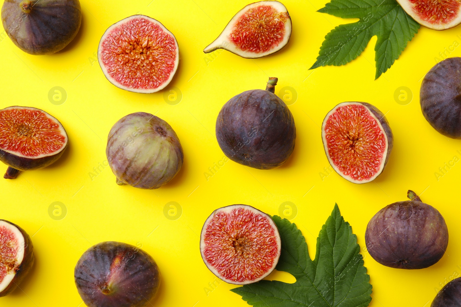 Photo of Fresh ripe figs with green leaves on yellow background, flat lay