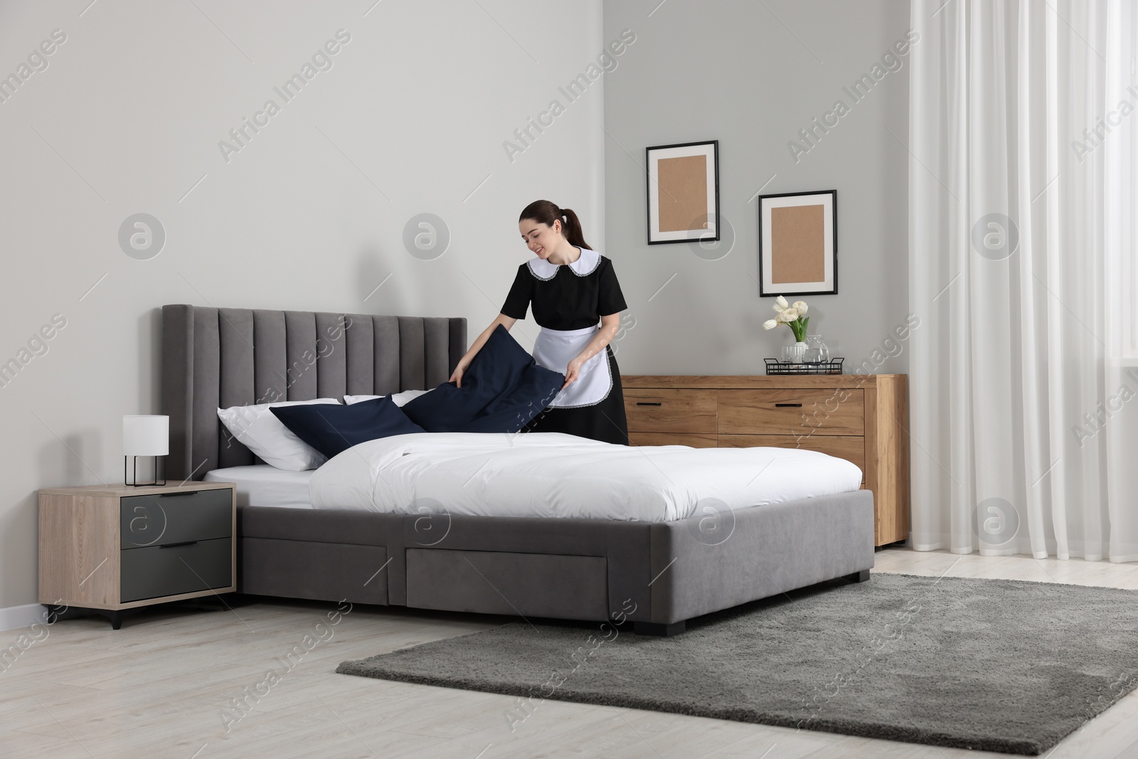 Photo of Young chambermaid making bed in hotel room