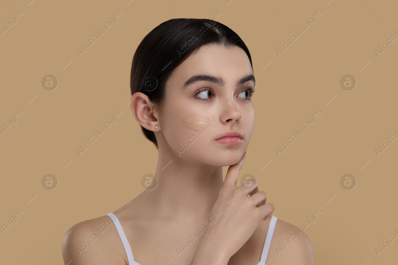 Photo of Teenage girl with swatch of foundation on face against beige background