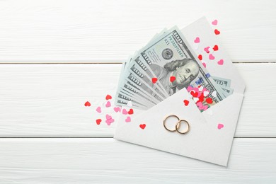 Honeymoon concept. Two golden rings, money and cutout hearts on white wooden table, flat lay. Space for text