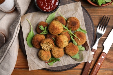 Photo of Delicious falafel balls with herbs and sauce on wooden table, flat lay