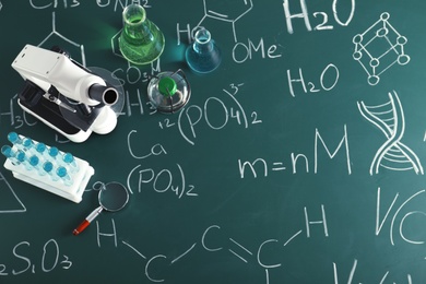 Laboratory glassware and microscope on blackboard with chemical formulas, top view