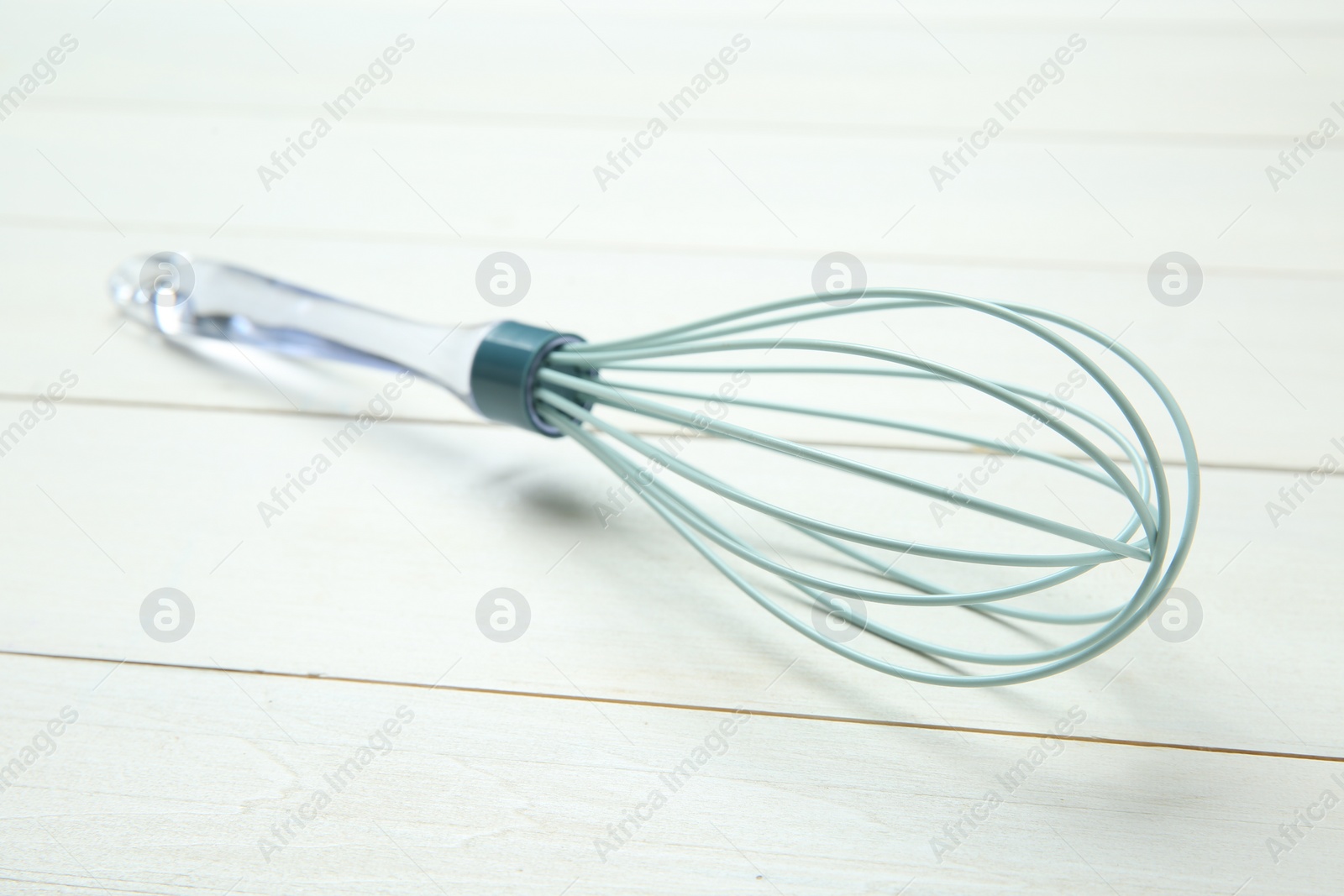Photo of One whisk on white wooden table, closeup