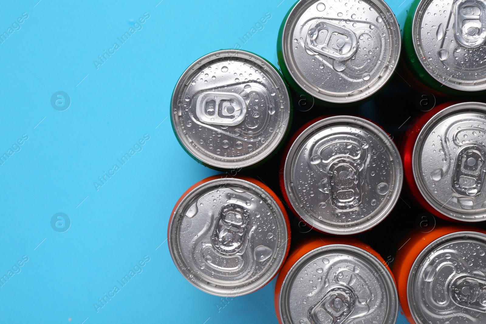 Photo of Energy drinks in wet cans on light blue background, top view. Space for text