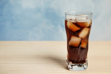 Photo of Glass of refreshing soda drink on wooden table against blue background, space for text