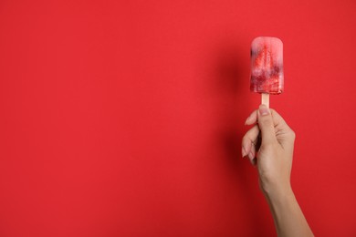Photo of Woman holding berry popsicle on red background, closeup. Space for text