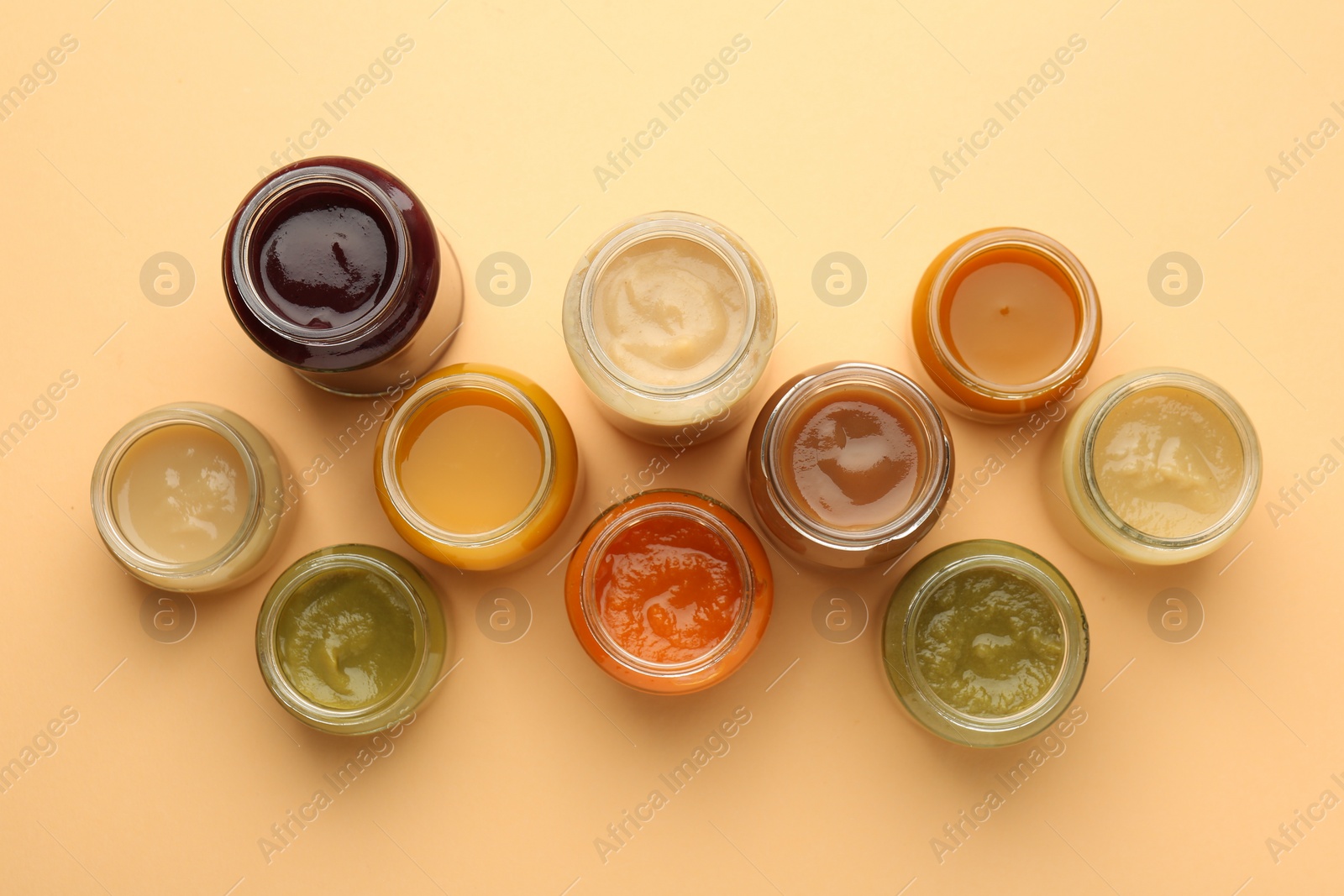Photo of Jars with healthy baby food on pale orange background, flat lay