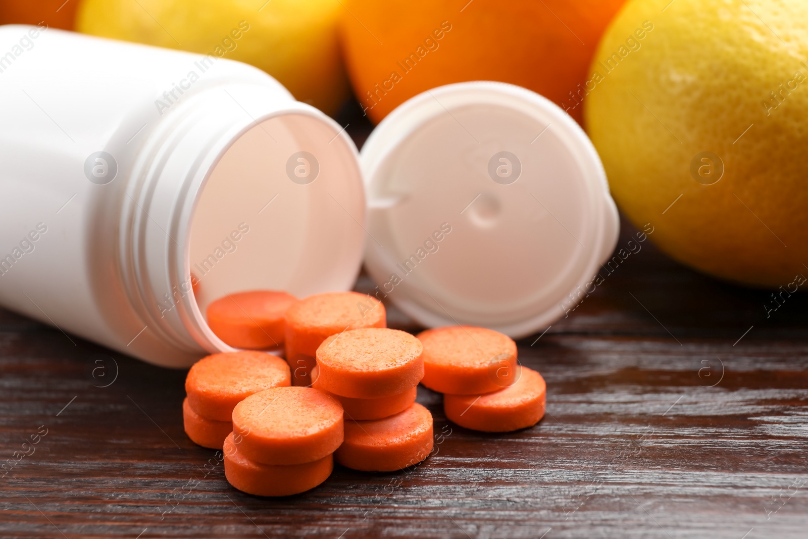 Photo of Dietary supplements. Overturned bottle, pills and fruits on wooden table, closeup