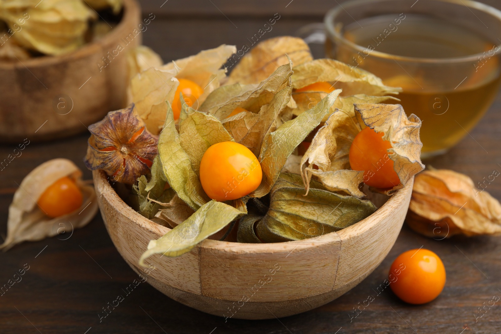 Photo of Ripe physalis fruits with calyxes in bowl on wooden table, closeup