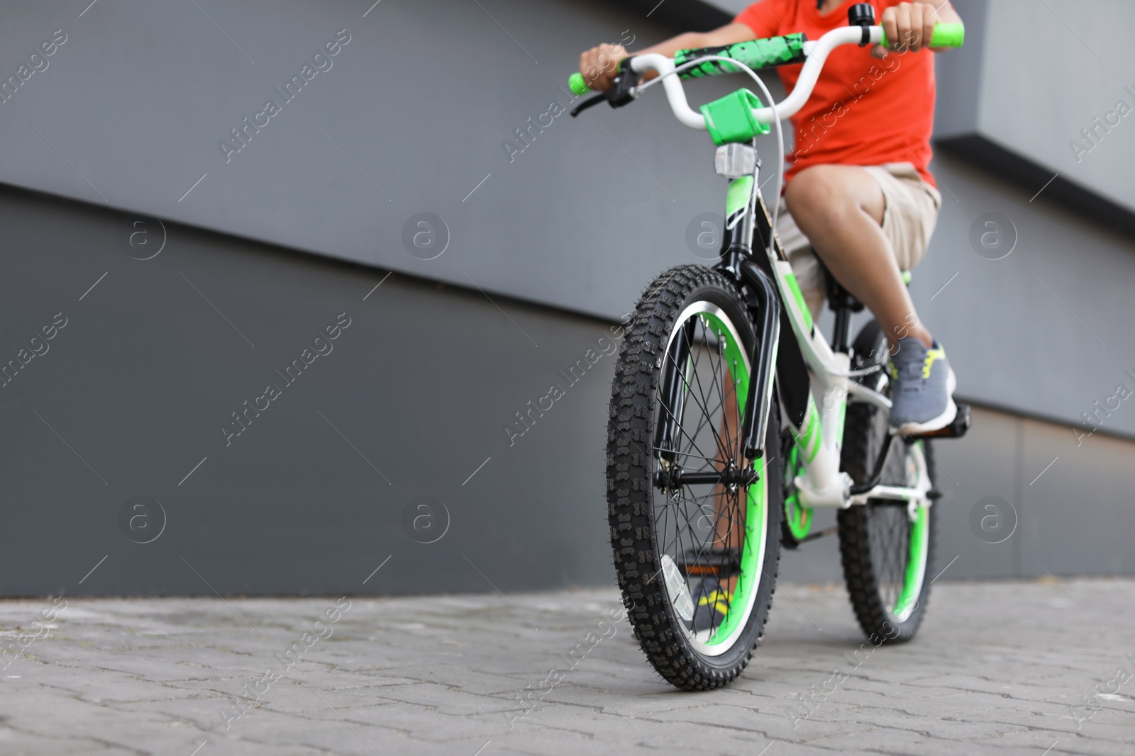 Photo of Little boy riding bicycle on street near gray wall, closeup