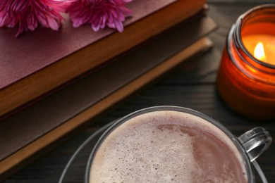 Photo of Cup with coffee, books and burning candle on wooden table, closeup. Morning ritual