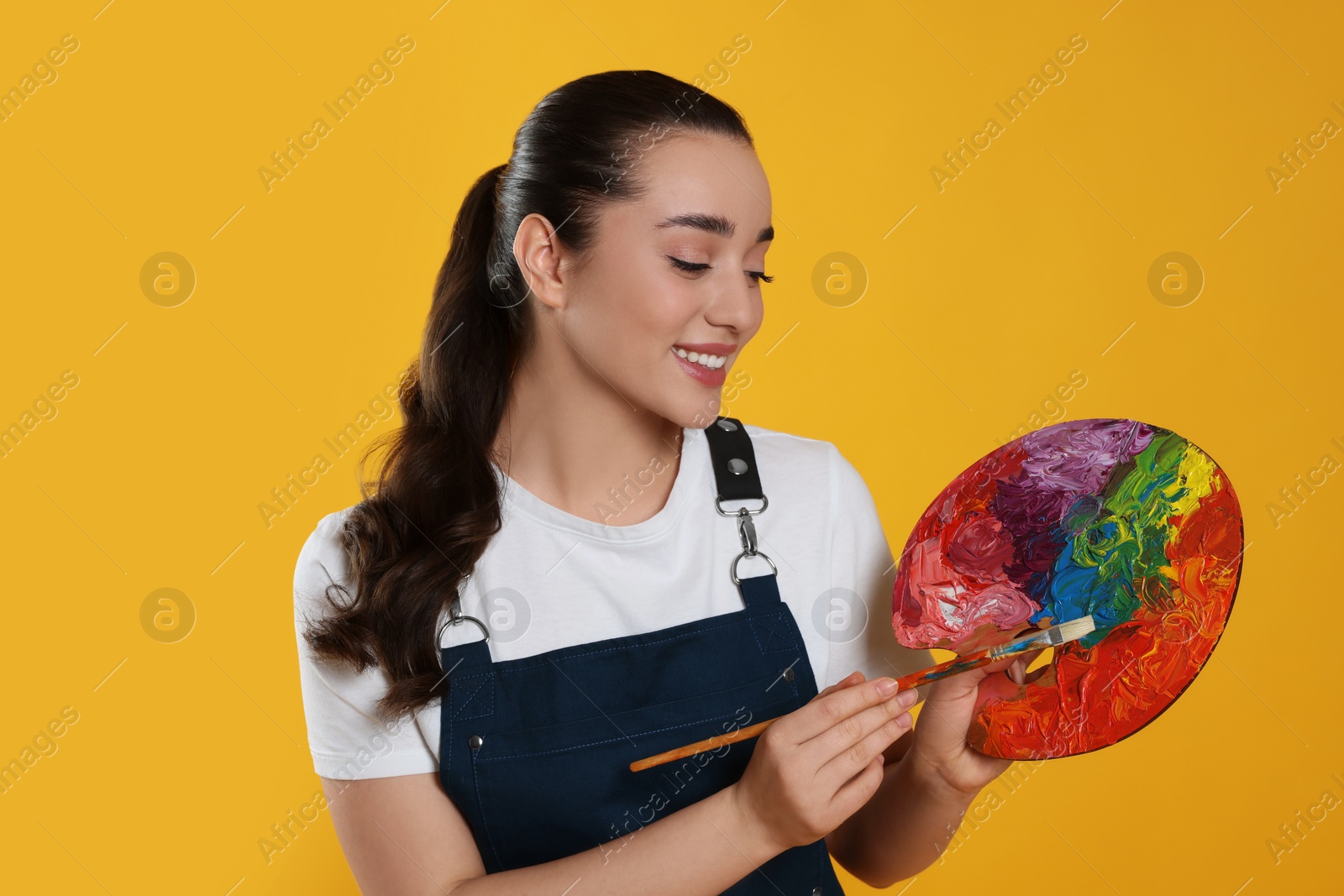 Photo of Woman with painting tools on yellow background. Young artist