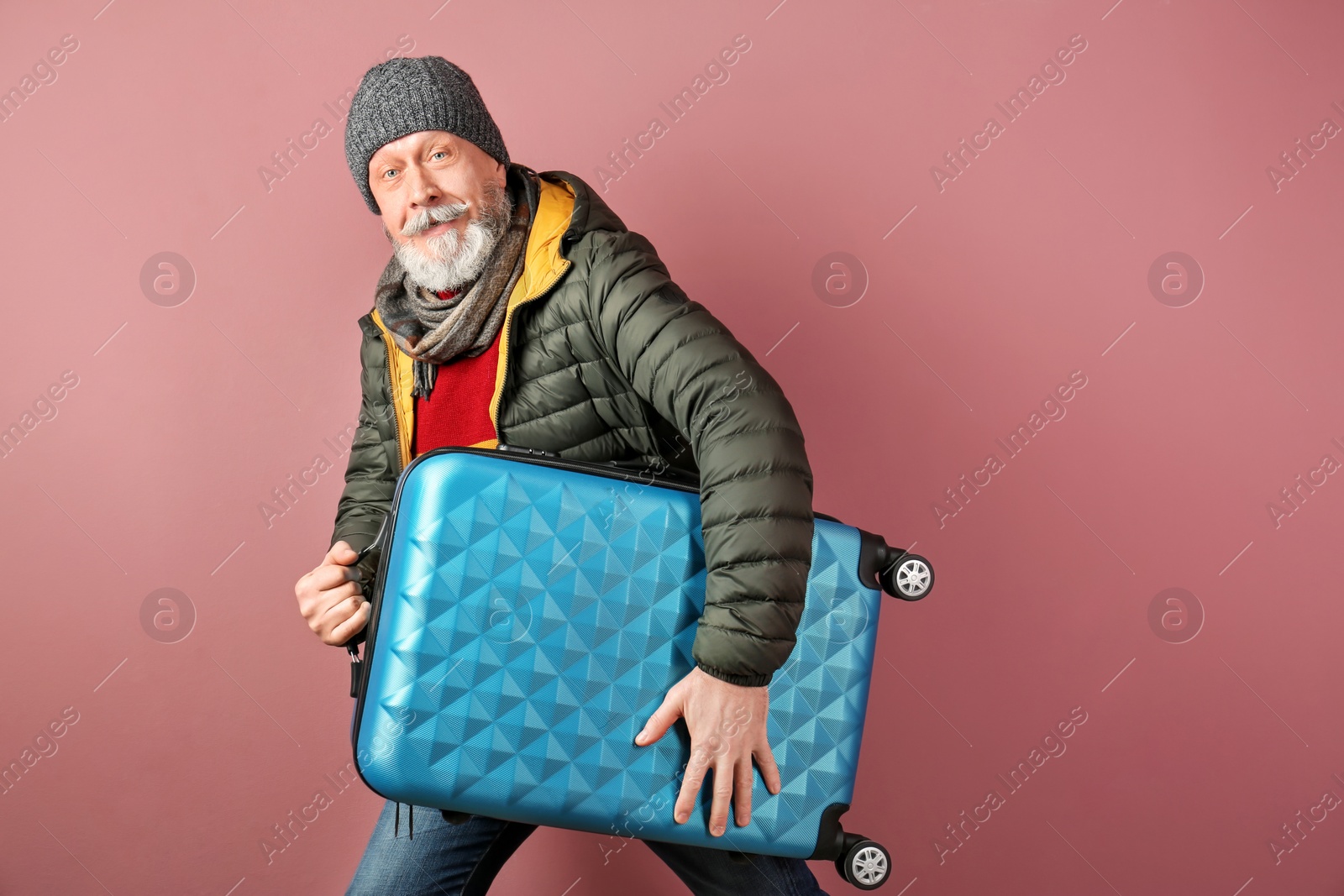 Photo of Mature man with suitcase on color background. Ready for winter vacation