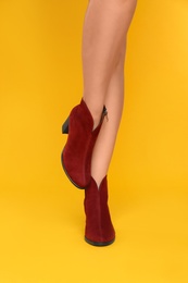 Photo of Woman wearing stylish boots on yellow background, closeup