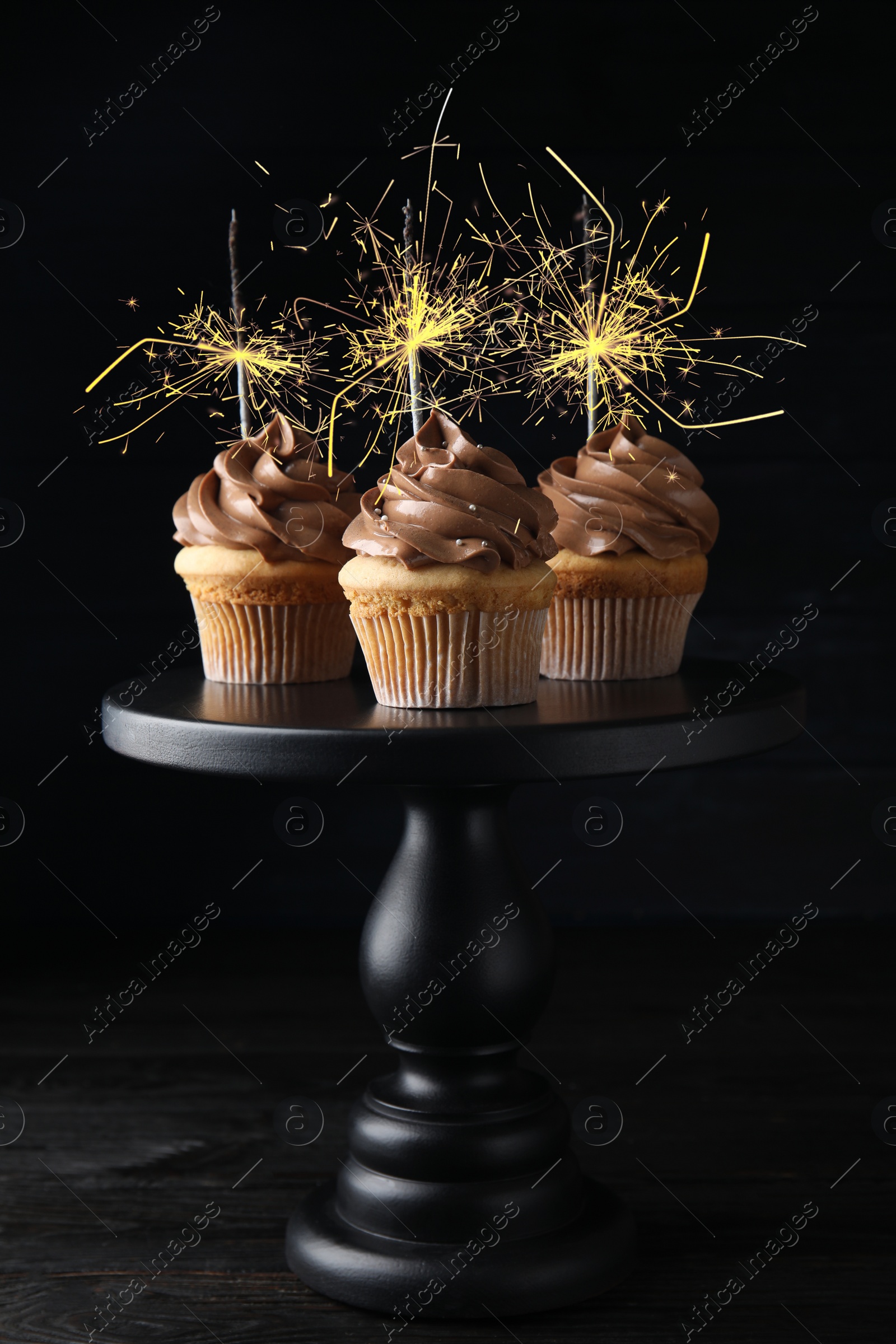 Image of Birthday cupcakes with sparklers on stand against dark background