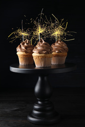 Birthday cupcakes with sparklers on stand against dark background