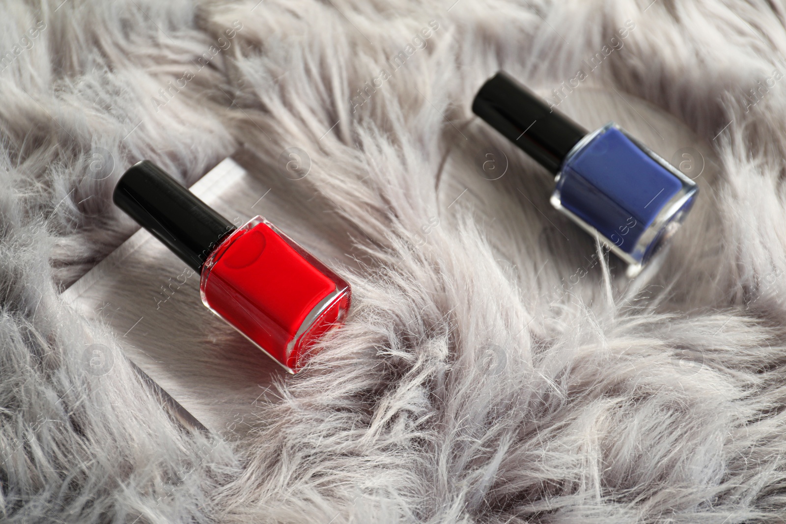 Photo of Bright nail polishes in bottles on grey faux fur, closeup